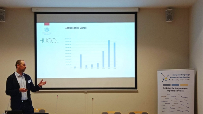 Jānis Ziediņš pie ekrāna prezentē platformas Hugo.lv izmantošanas statistiku
