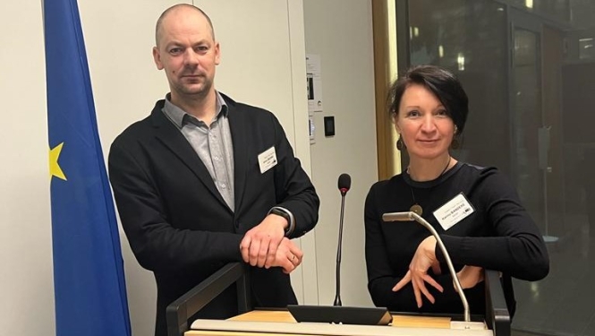 Jānis Ziediņš un Karīna Bandere pie referenta pults ar Eiropas Savienības karogu